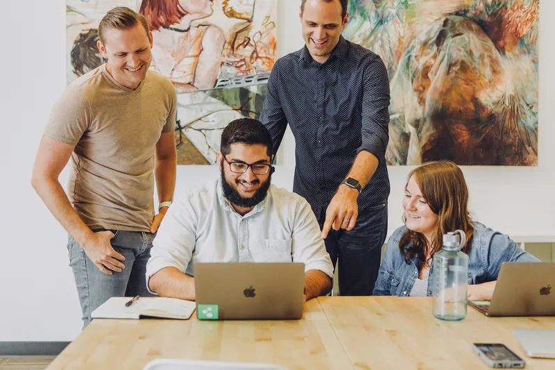 Four colleagues smiling around a laptop at work